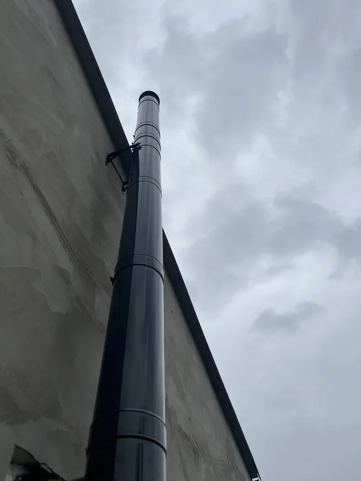 Černý nerezový komín vedený podél štítové stěny domu proti obloze