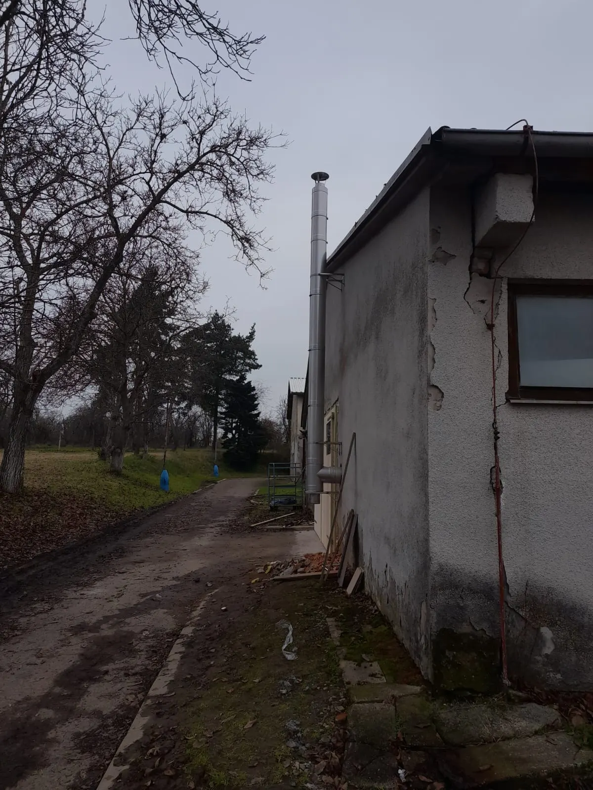 Zděný komín s hlavou nad střechou venkovského domu, kde se topí dřevem