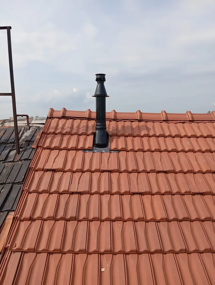 Černé odkouření kotle procházející novou taškovou krytinou u&nbsp;hřebene střechy
