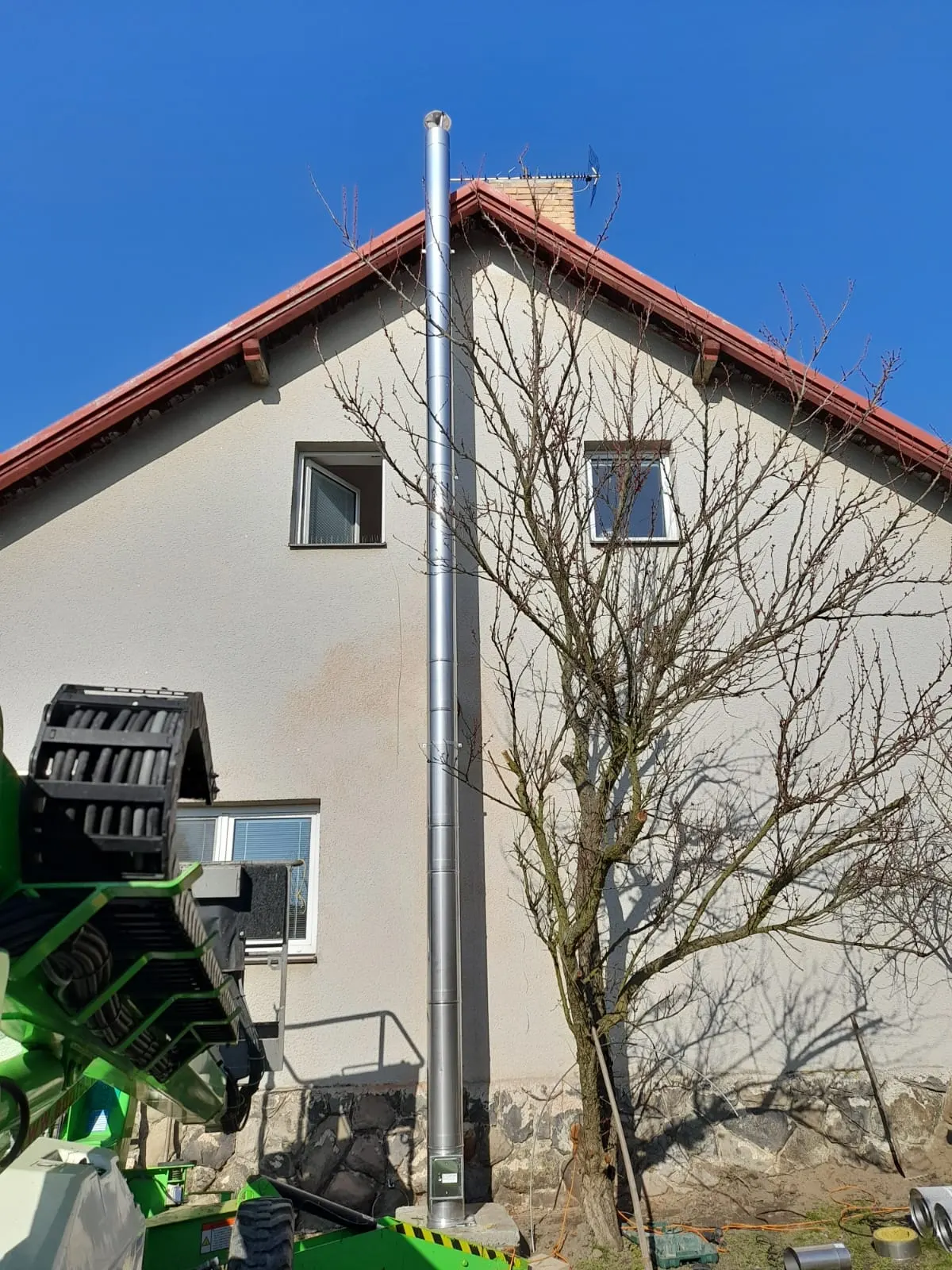 Třísložkový nerezový komín vedený po štítové stěně domu nad hřeben střechy